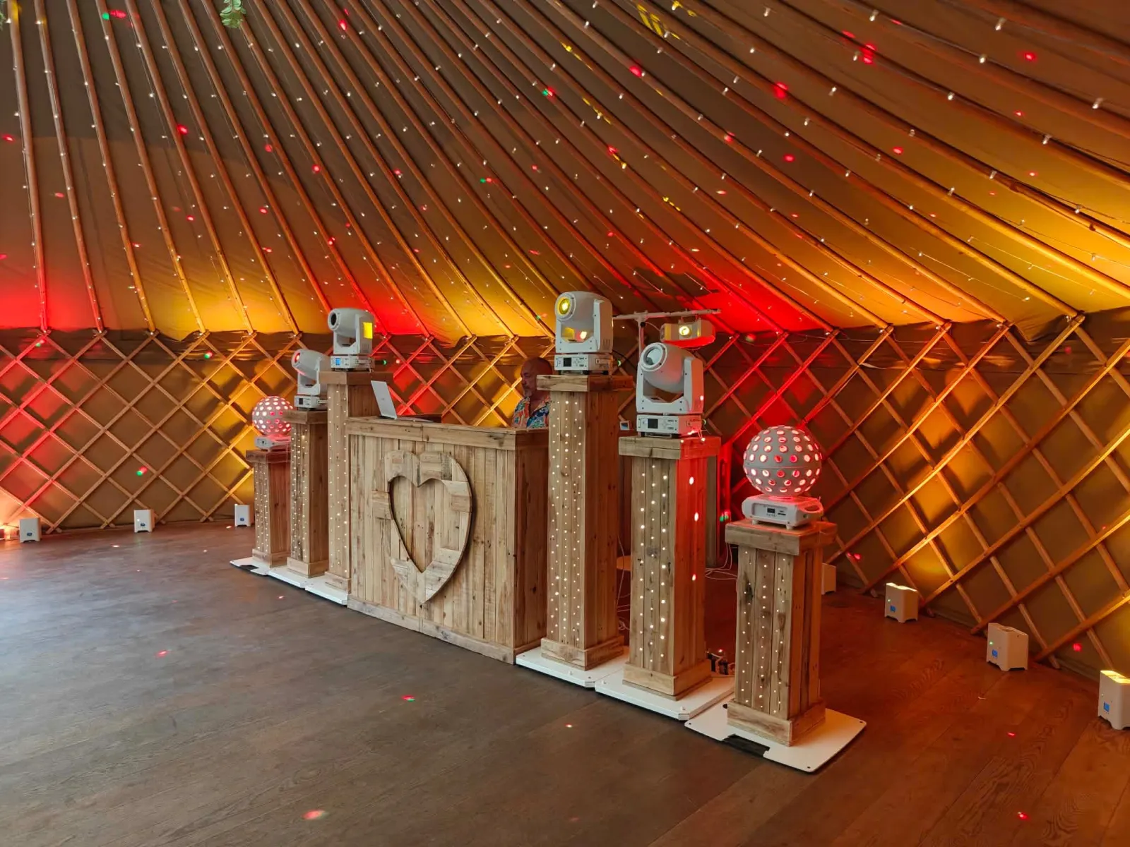 Rustic wooden DJ booth with heart centrepiece and moving-head lighting inside a yurt